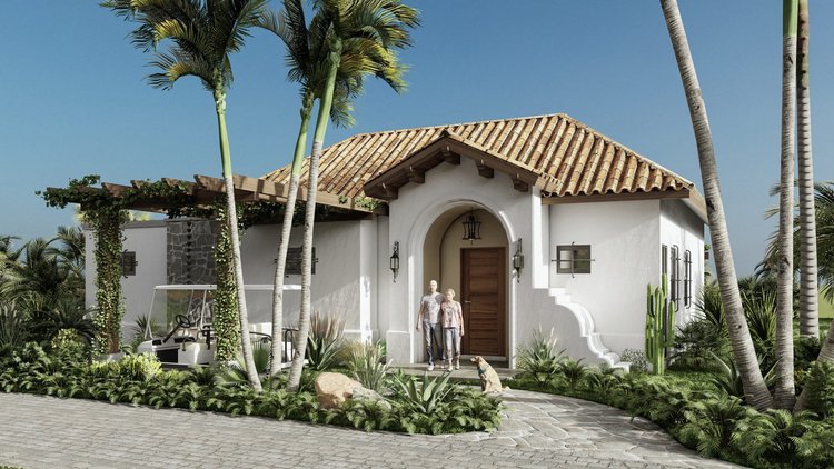 A white house with a clay tile roof surrounded by palm trees and tropical plants, with two people and a dog standing at the front door.